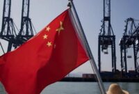 1765105568233-sebuah-bendera-china-yang-sedang-berkibar-di-depan-mesin-pengangkut-kargo-di-pelabuhan-di-china_169